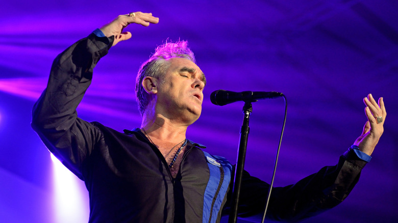 Morrissey sur scène sous une lumière violette avec microphone