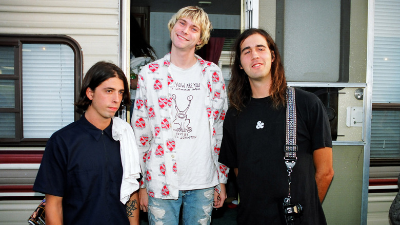 Dave Grohl, Kurt Cobain et Krist Novoselic, membres de Nirvana, sourient et posent ensemble devant une caravane