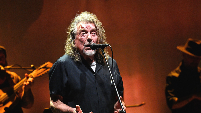Robert Plant en chemise sombre sur scène avec microphone
