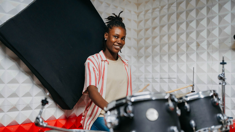 Jeune femme assise devant un kit de batterie tenant des pilons