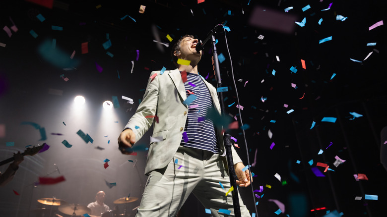 Damian Kulash d'OK Go chante dans un micro sur scène tandis que des confettis arc-en-ciel pleuvent d'en haut