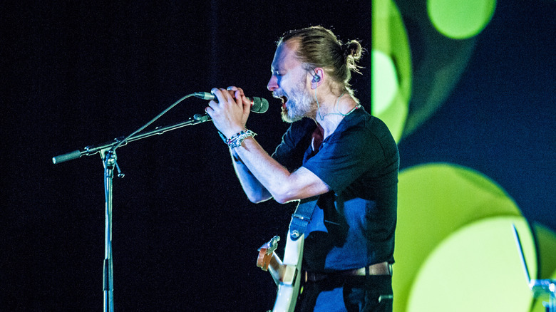 Thom Yorke tient un microphone à deux mains tandis que des cercles verts flottent sur scène derrière lui lors d'un concert à Amsterdam en 2018.