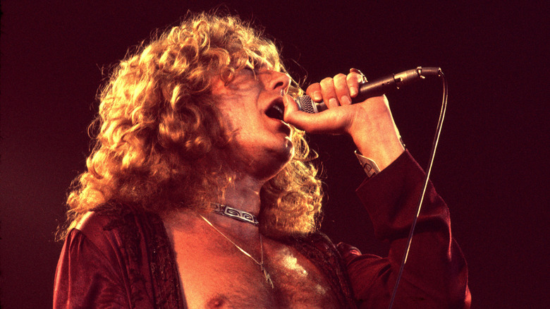 Robert Plant chantant sur scène en 1977 portant un tour de cou gravé en argent, un chemisier ouvert rouge brodé et un pendentif paratonnerre