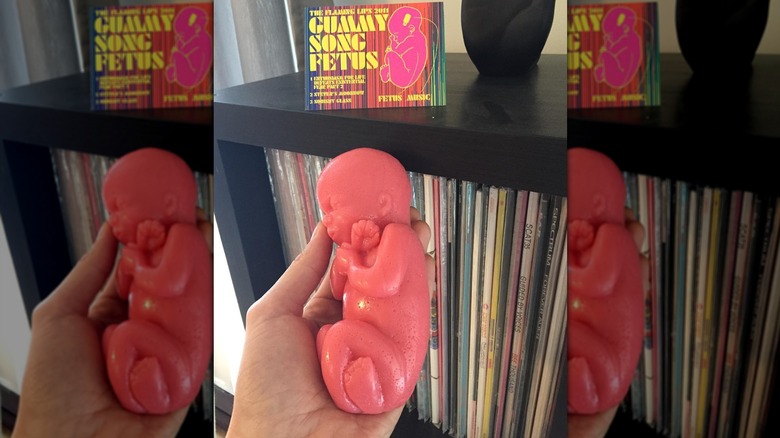 Une main tenant Flaming Lips "Fœtus de chanson gommeuse," un fœtus fait de bonbons gommeux