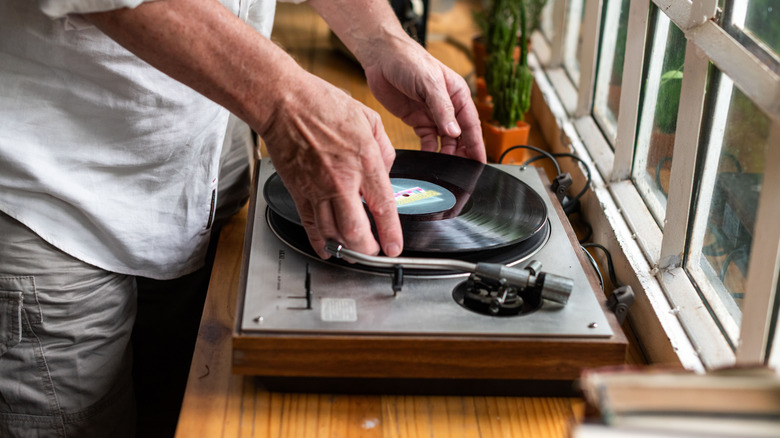 Un homme plaçant un disque vinyle sur une platine près de la fenêtre.