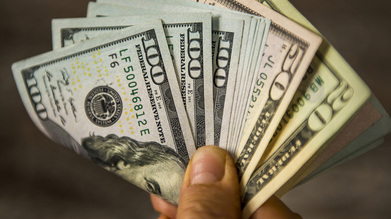 Une main tenant des billets pliés en dollars américains.